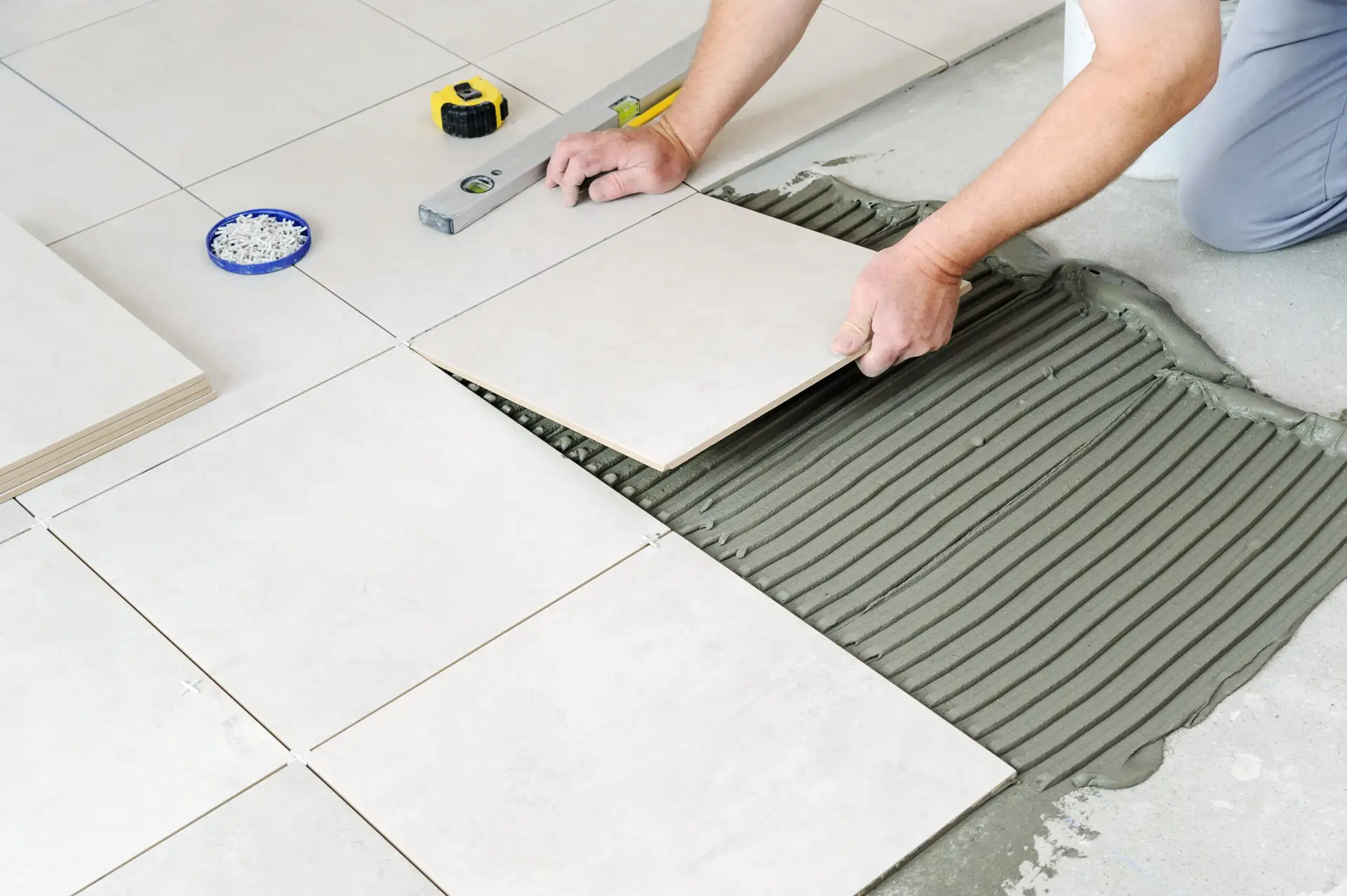 White, ceramic tile being laid on the floor by a professional tile installer.