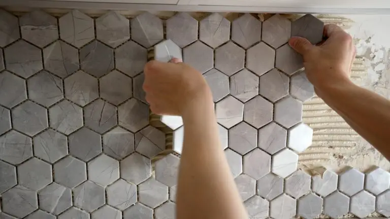 Hexagonal, grey mosaic tile is being placed vertically on a wall by professional tile installers.