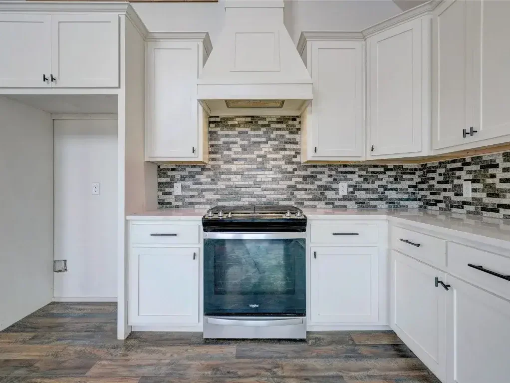 A kitchen with white cabinets, new tile backsplash, and new tile flooring.