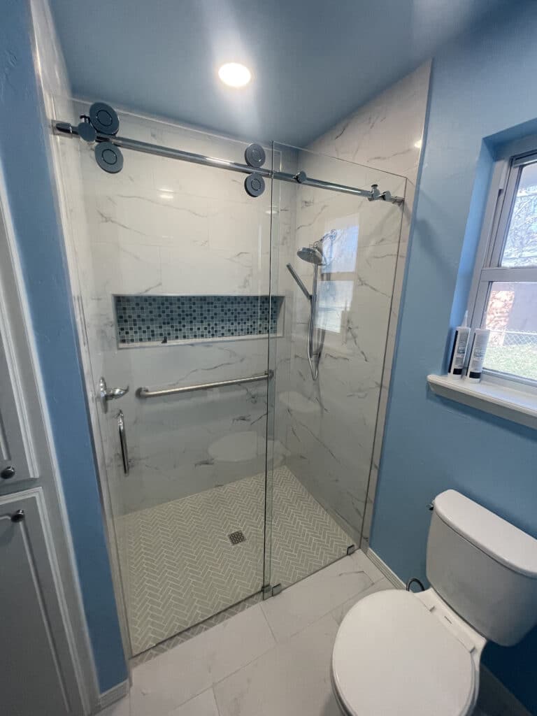 Completed bathroom remodel by Tile Genie of Oklahoma showing off a new shower, toilet, and painted blue walls.
