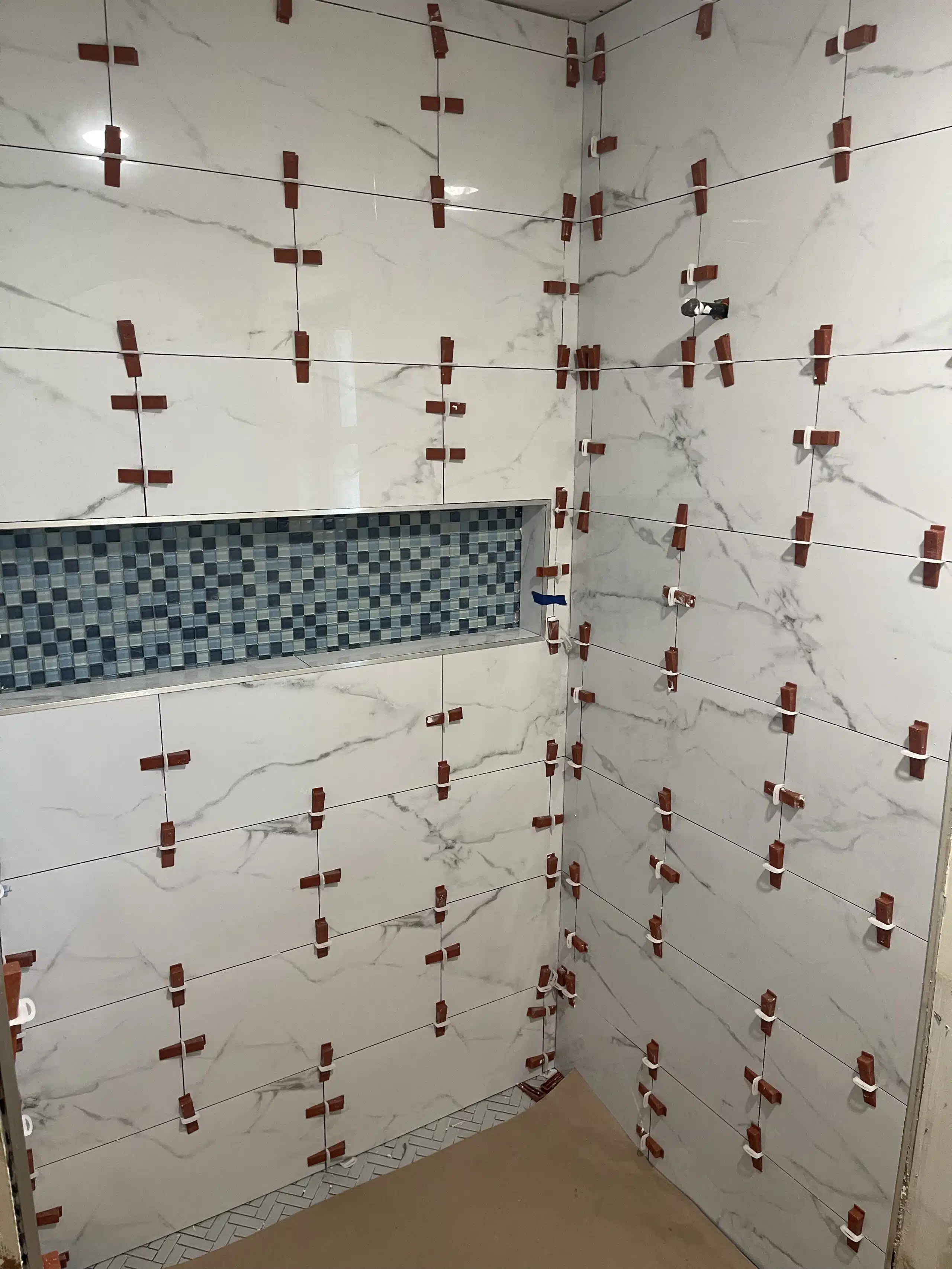 White shower tiles with red spacers are shown as part of a bathroom tile install and remodel from The Tile Genie of Oklahoma.